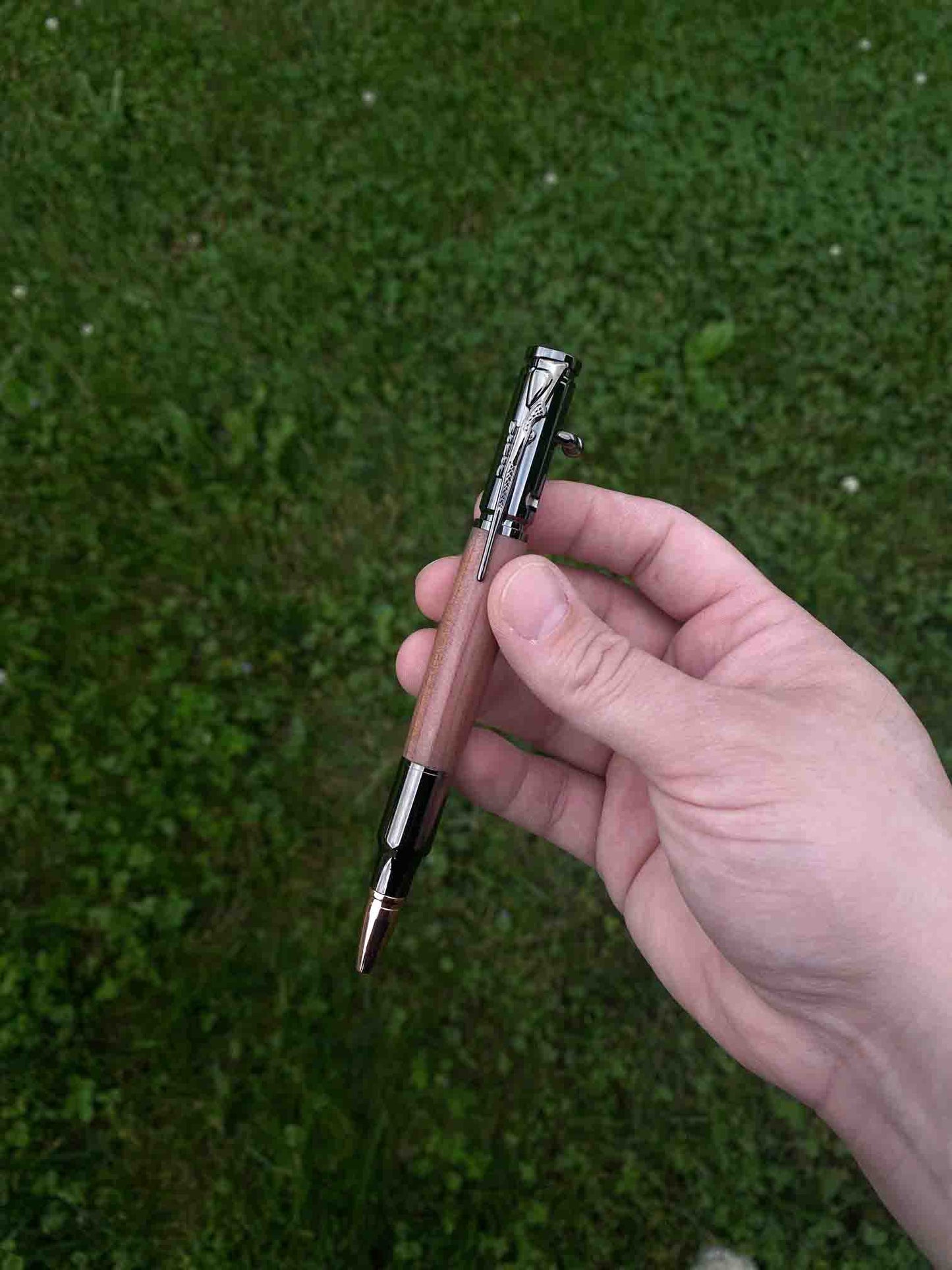 Our Cedarwood Bolt Action Ballpoint Pen, held by one of our Maker's against a grassy backdrop